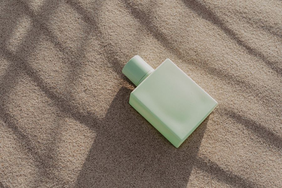 Sage green coated perfume bottle on sand