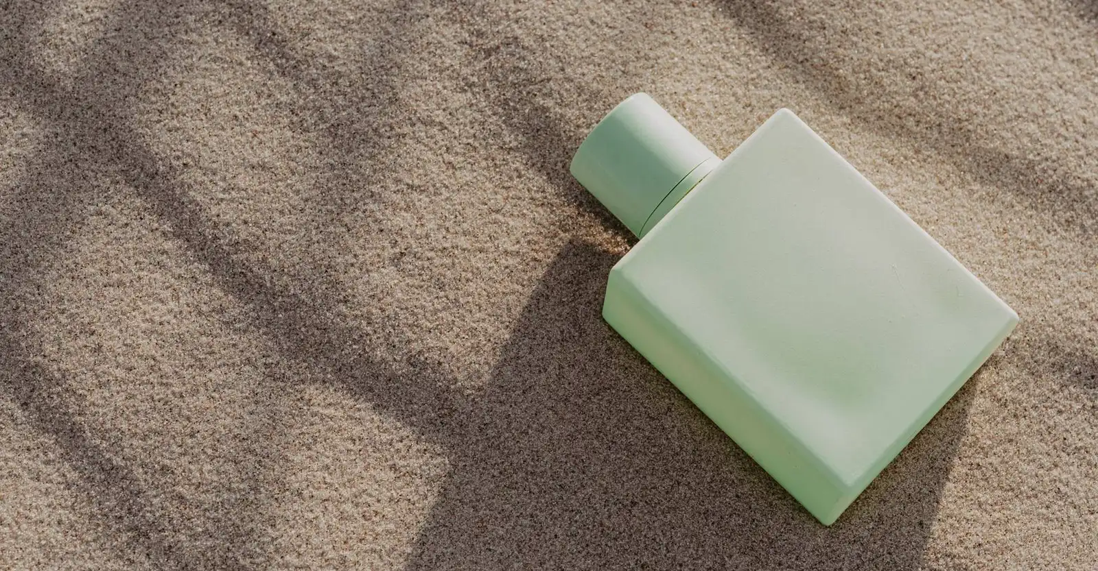 Sage green coated glass perfume bottle on sand